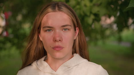 young lady with bold expression, gazing directly at camera in natural setting, sunlight casts gentle shadows across her face, blending with lush green background