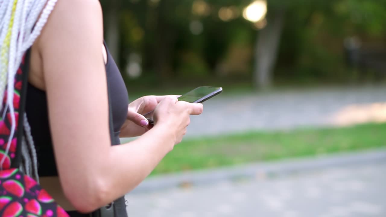 스마트 폰을 사용하여 배 ⁇  메시지를 가진 인식 할 수없는 소녀. 길을  ⁇ 는 dreadlocks와 여성, 느린 녹색 공원