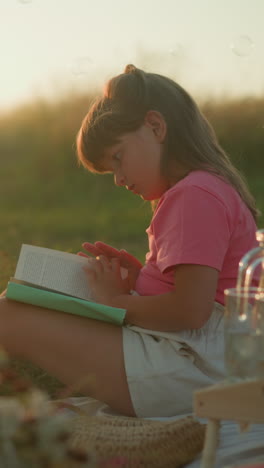 niña pequeña sentada al aire libre durante la hora dorada leyendo un libro, rodeada de preparación de picnic con frutas y croissant, la cálida luz dorada del sol llena el fondo mientras las burbujas flotan suavemente en el aire