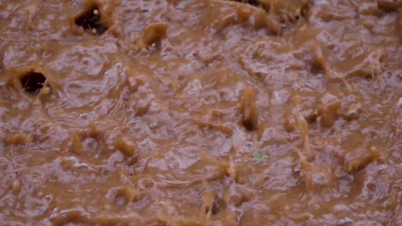 un primer plano de una fuerte lluvia cayendo sobre un charco fangoso y creando salpicaduras