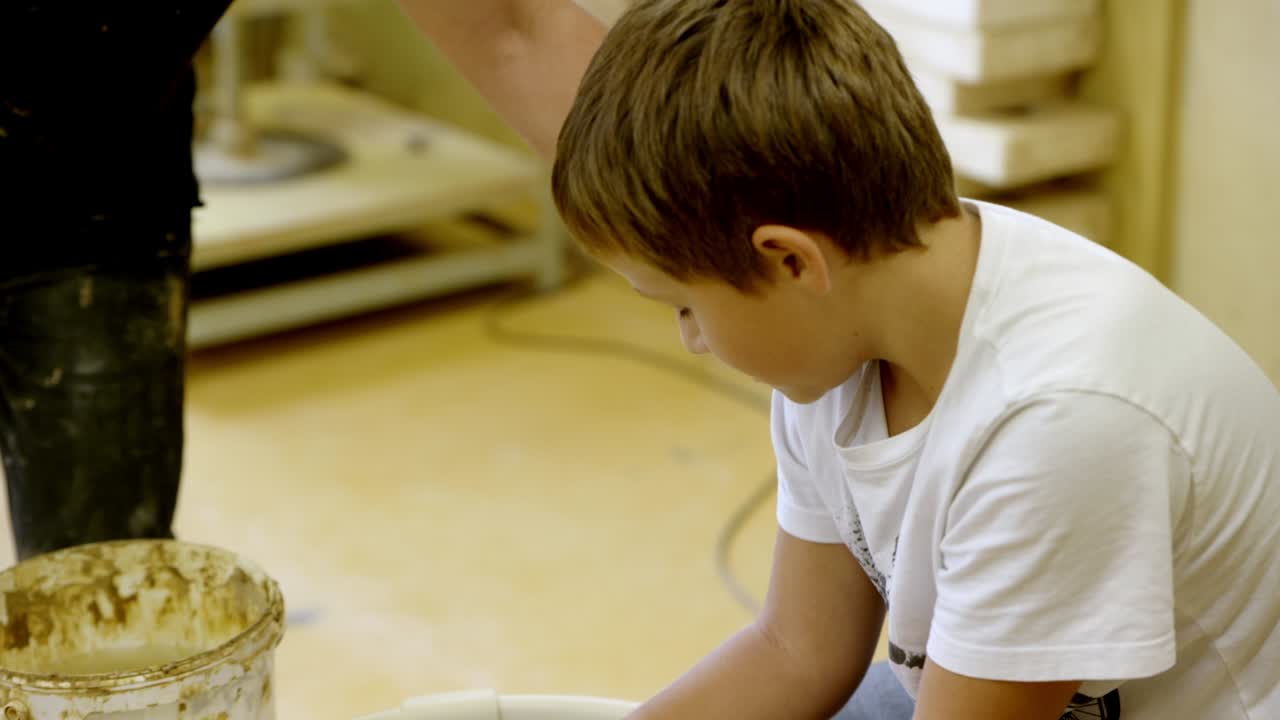 The teacher instructs the pupil while working with clay on the potter's wheel