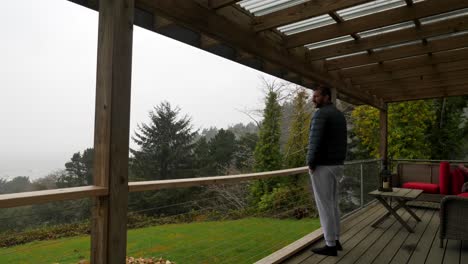 Static-view,-man-with-beard-looks-at-ocean-from-garden-terrace-on-deck,-on-rainy-cloudy-day