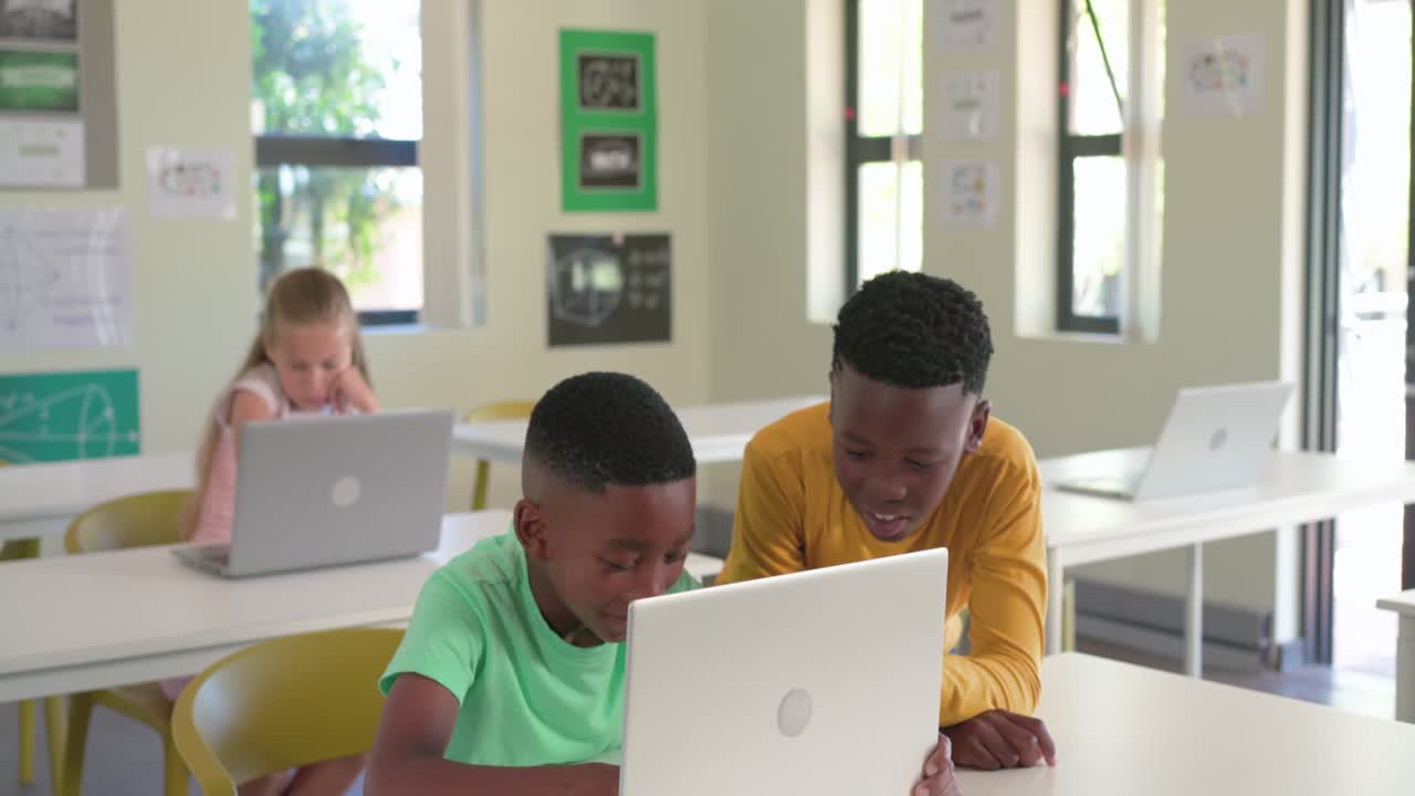 Two African American teenage boys opening laptop, collaborating during class, typing and cheering
