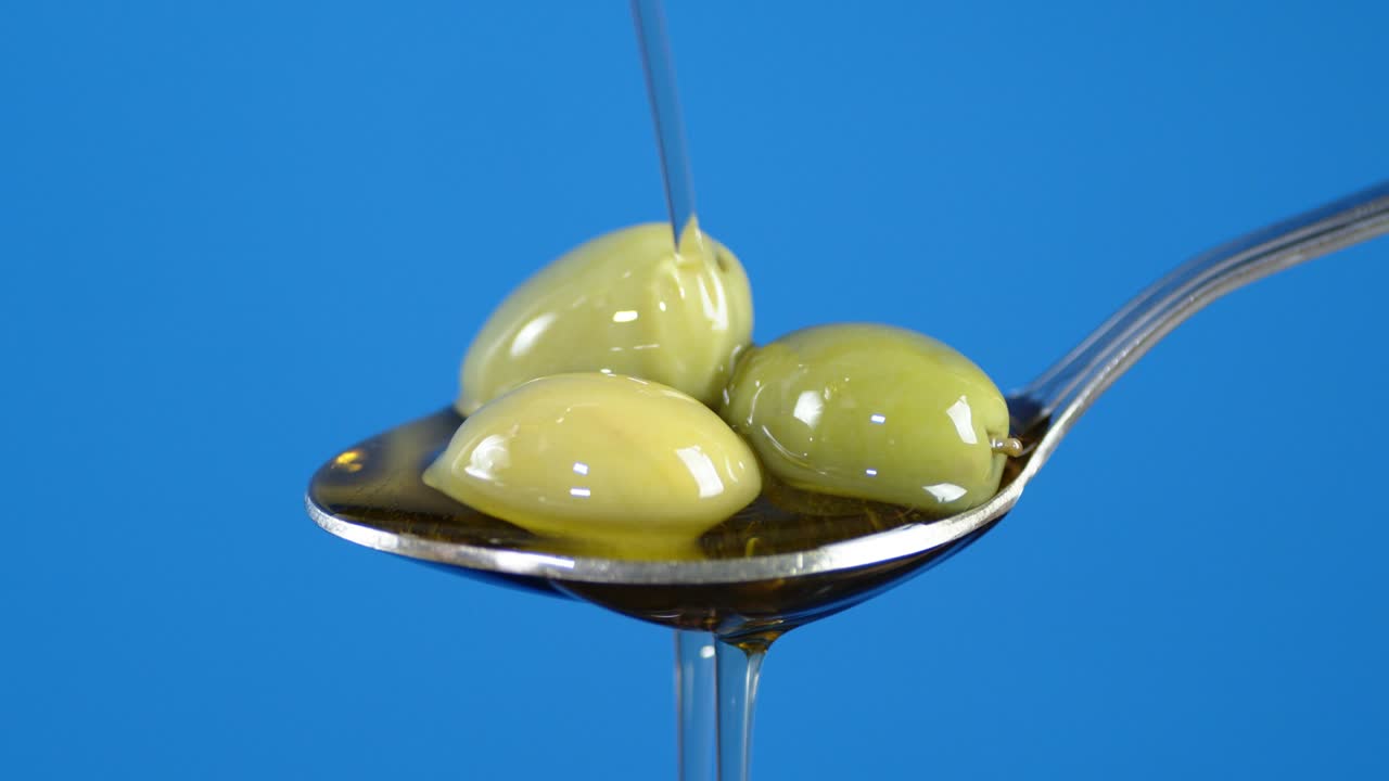 The olives are in a spoon of pouring olive oil.
