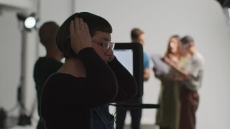 rear view of film crew shooting movie or video in studio with female director talking with actors in rehearsal