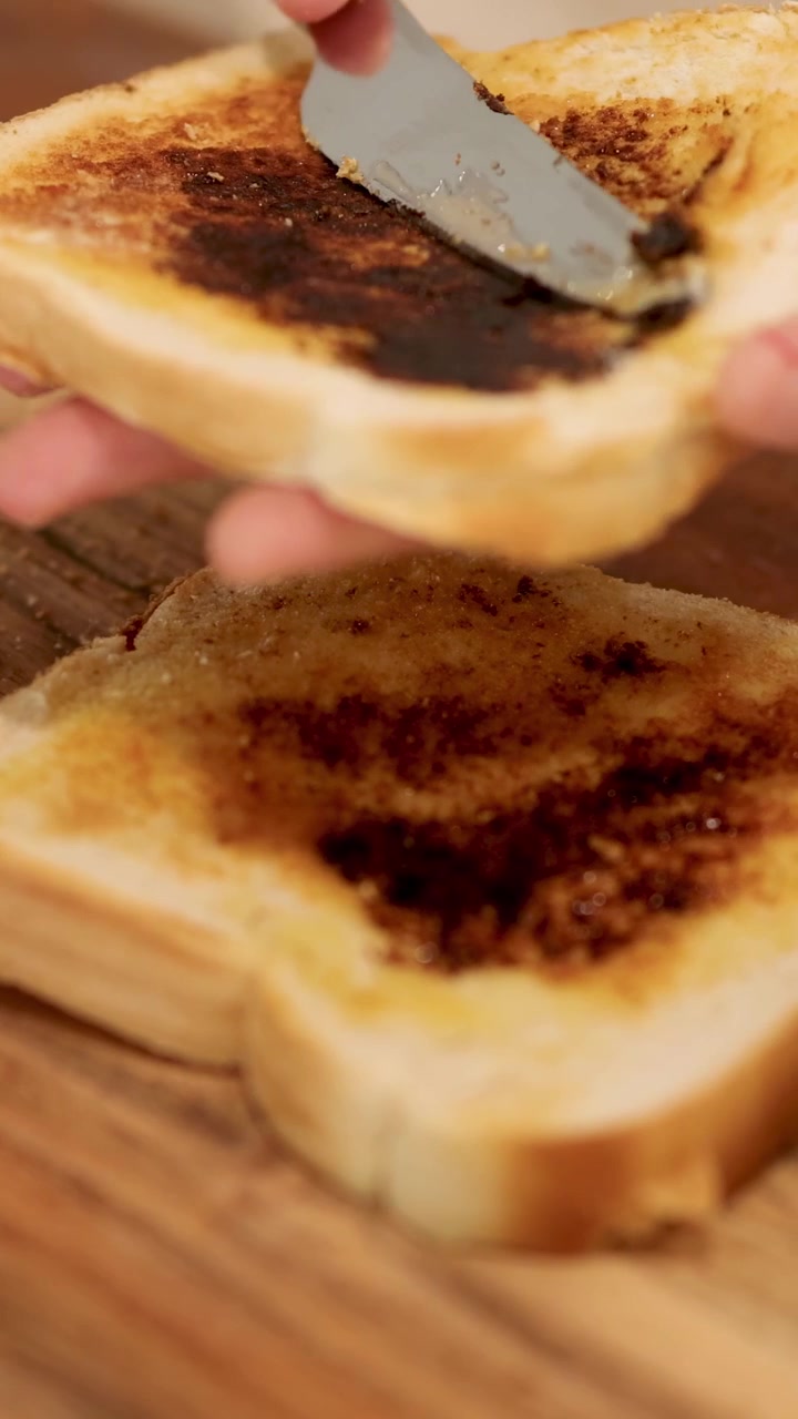 A person spreads Vegemite on toast in a well-lit kitchen, showcasing a simple breakfast preparation