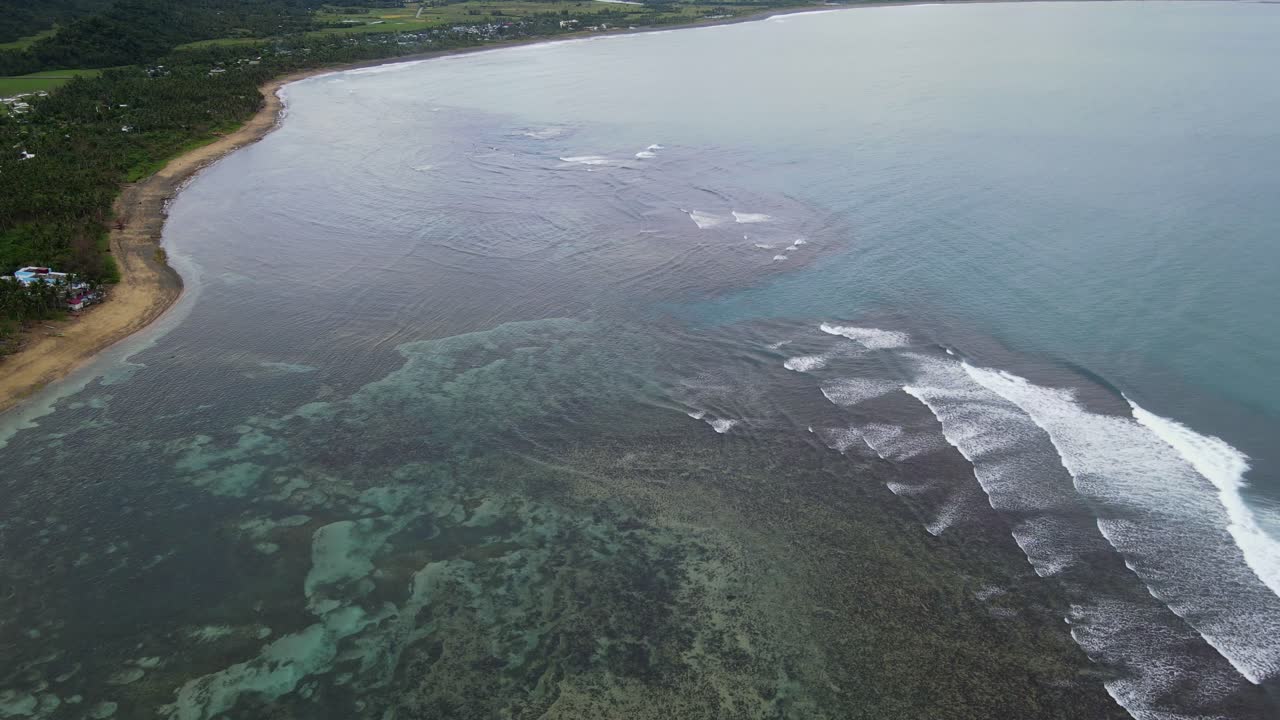 Panoramic aerial flyover shot of tidal waves crashing against fringing reefs along tropical island coastline at Virac, Catanduanes, Philippines