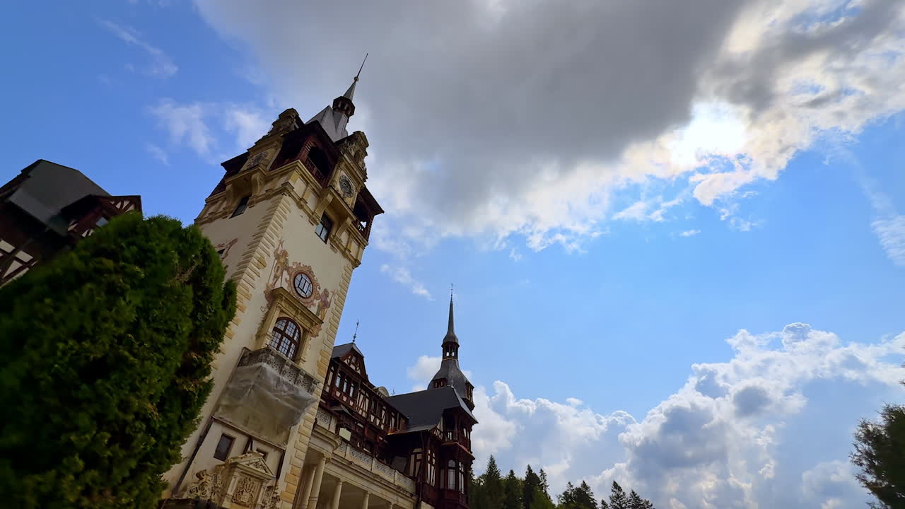 Avvicinamento alla torre dell'orologio dello splendido Castello di Peleș, nella contea di Prahova, Romania. Angolo di ripresa dal basso. Nuvola grigia nel cielo azzurro sullo sfondo