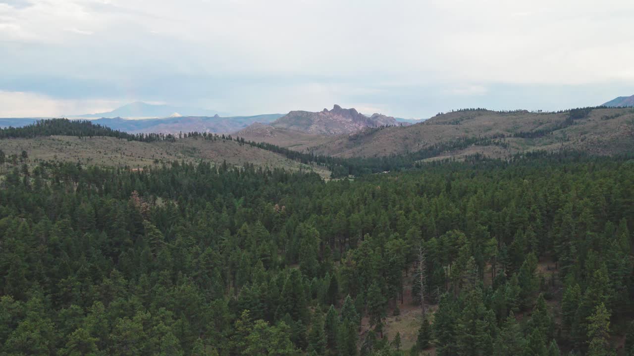 Lento volo di un drone con nuvole cupe sopra una remota foresta montana con area selvaggia e scogliere rocciose in lontananza. Filmato nel Pike National Forest del Colorado