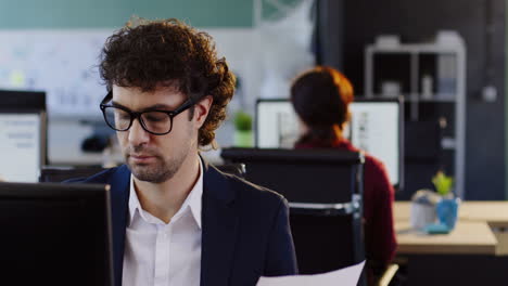 caucasian businessman in glasses working on computer and reading a document in the office