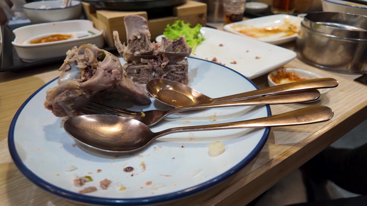 Close-up of finished meal with beef rib bones and silverware on a restaurant table.