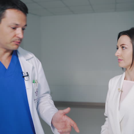 doctors in medical clothing go out from lift in a modern private clinic. doctor man is talking to a female physician in the light corridor in hospital.