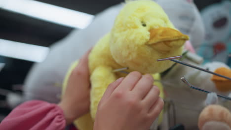 dama de rosa toca suavemente un juguete de peluche amarillo en un estante de la tienda, rodeado de otros animales de peluque, el juguete es con efecto de luz borrosa, mientras lo inspecciona cuidadosamente, en una tienda bien iluminada