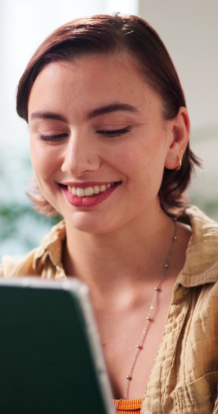 明るい室内でタブレットを使い、笑顔を見せる若い女性