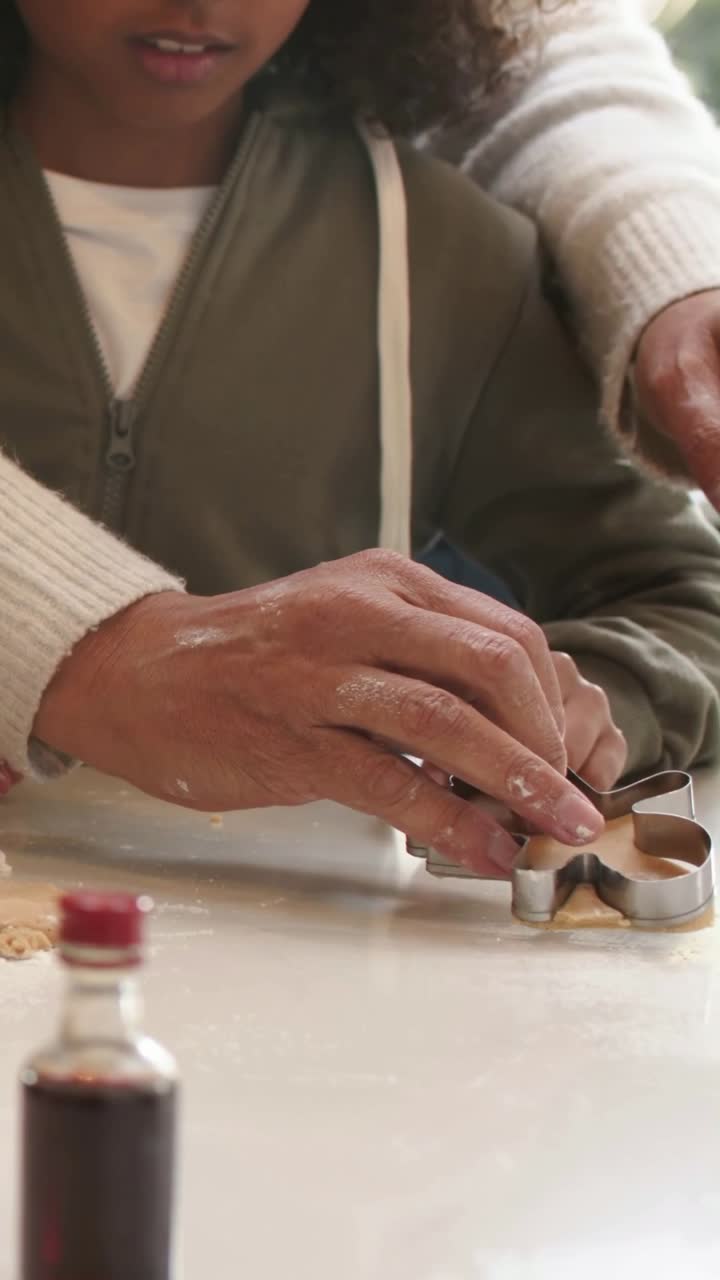 Video verticale: Bambino con felpa verde oliva che posiziona lo stampino per biscotti con un adulto che aiuta a casa per fare i biscotti
