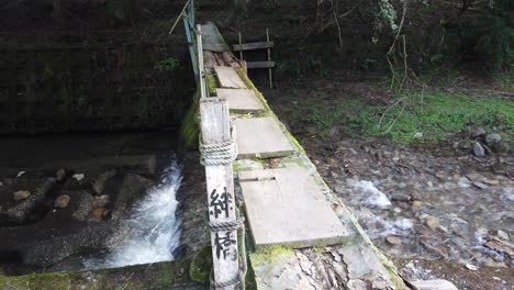 Japón-Madera-Antiguo-Puente-Cruzando-Hacia-El-Bosque-Oscuro-Agua-Río-Flujo-Piedra-Kanji