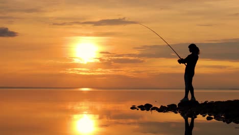 Frau-Fischt-Auf-Angelrute,-Die-Sich-Bei-Sonnenuntergang-Im-Hintergrund-Dreht.