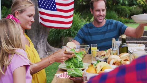 pareja caucásica sonriente sirviendo a la familia teniendo una comida de celebración juntos en el jardín