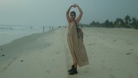 A-tan-woman-stands-on-a-beach-with-her-arms-outstretched