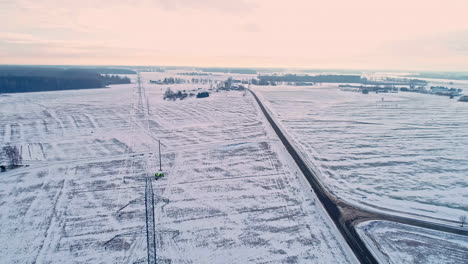 Trabajador-Industrial-Que-Repara-La-Torre-De-Transmisión-Durante-El-Día-Nevado-De-Invierno-Por-La-Mañana---Vuelo-Aéreo-Hacia-Atrás