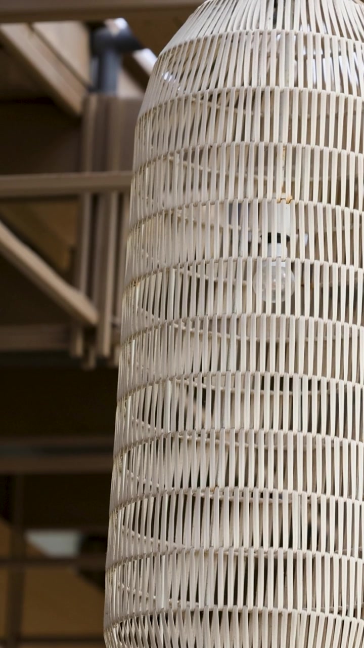 Un ventilatore a soffitto gira lentamente in un atrio luminoso e moderno di un hotel con arredamento in vimini e illuminazione naturale.