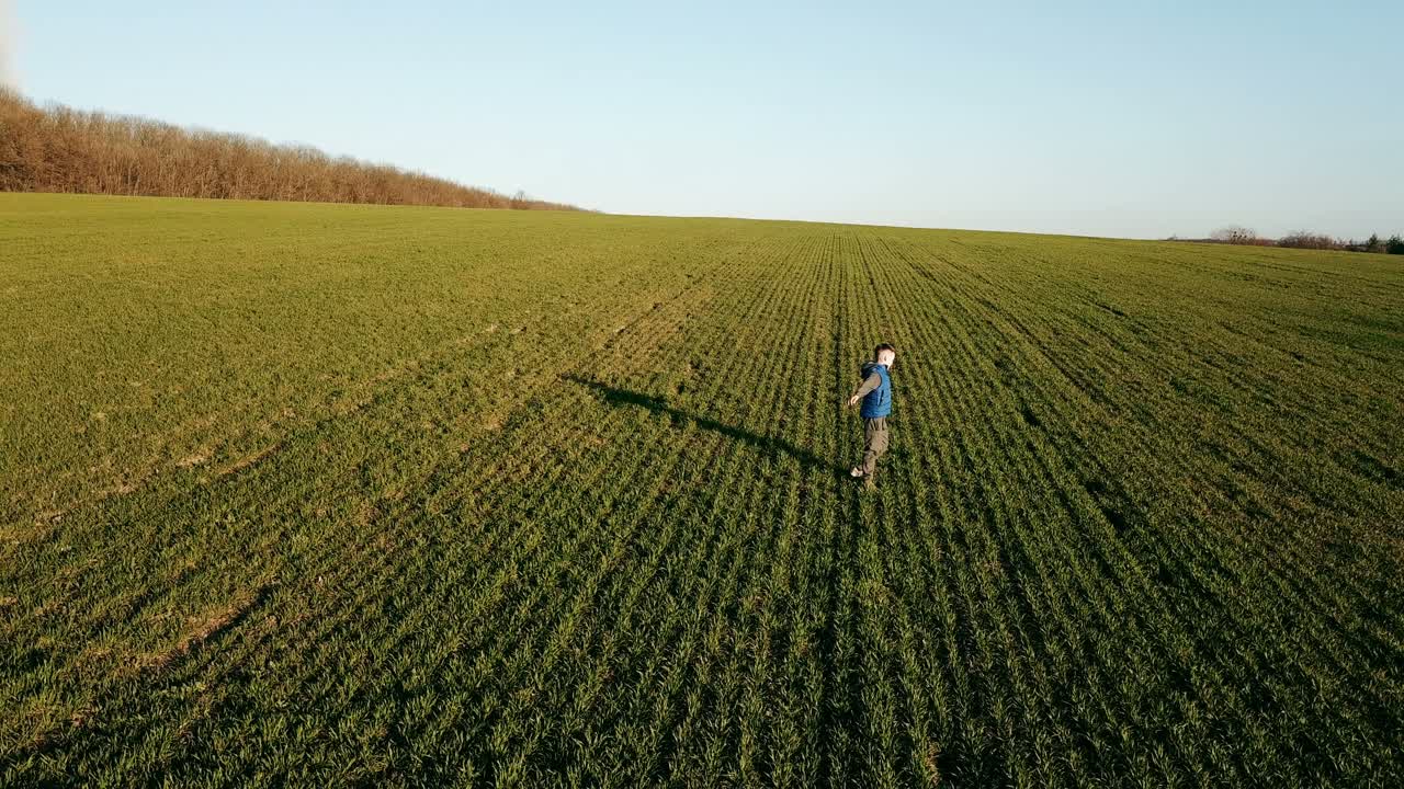 Un bambino con un gilet blu sta girando in mezzo a un campo sullo sfondo di un paesaggio estivo