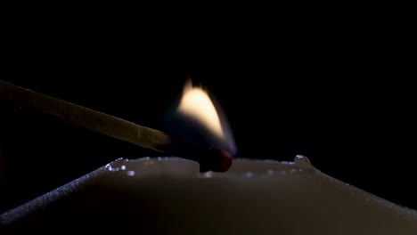 imágenes macro en cámara lenta de una vela blanca encendida por un fósforo sobre un fondo oscuro