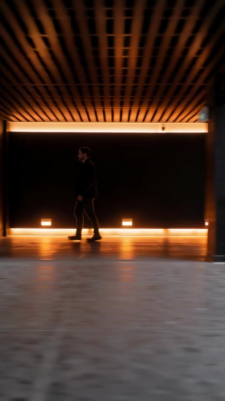 Vertical video: Walking man in dark coat moving to exit across atrium, camera panning past column