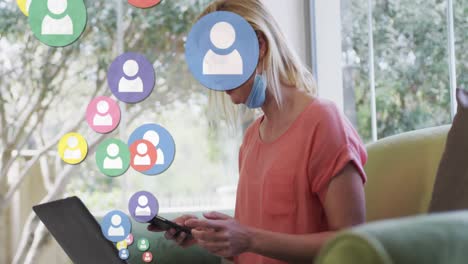 animation of digital icons over caucasian woman in face mask using smartphone at home