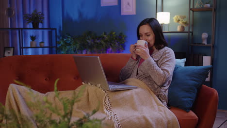 mujer independiente acostada en el sofá, trabajando en una computadora portátil, comprando, estudiando en línea en casa sola