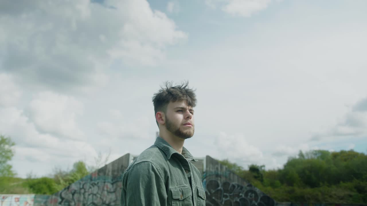 Medium shot of young man beside basketball court, cloudy background and grass foreground