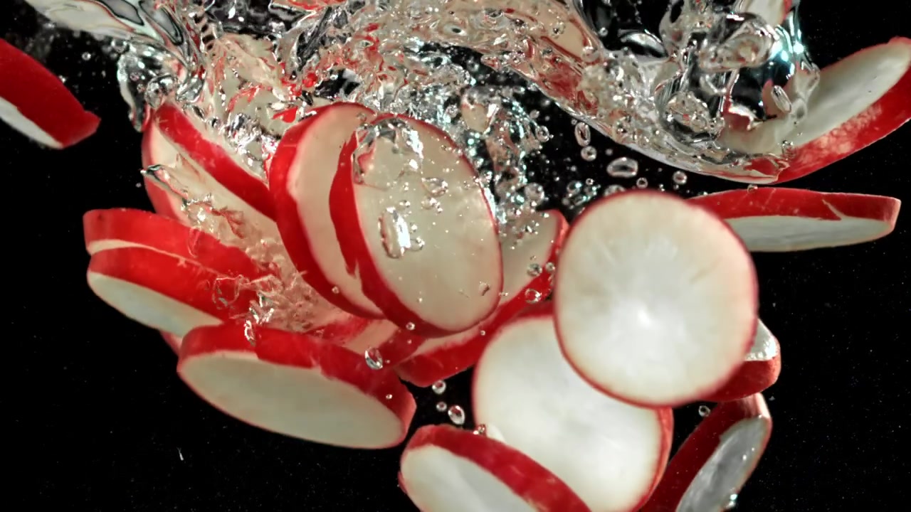 Radis tranchés tombant dans l'eau avec des bulles sur fond noir