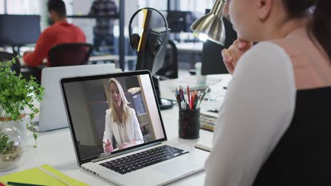 Caucasian-woman-having-a-video-call-on-laptop-with-female-colleague-at-office