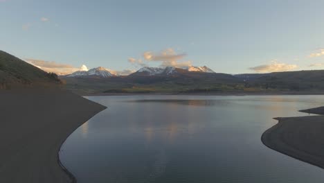 Hermosa-Puesta-De-Sol-Volar-Lentamente-Sobre-El-Establecimiento-De-Tiro-Sobre-La-Ladera-De-La-Montaña-En-Las-Montañas-Rocosas-Cubiertas-De-Nieve-Y-El-Lago