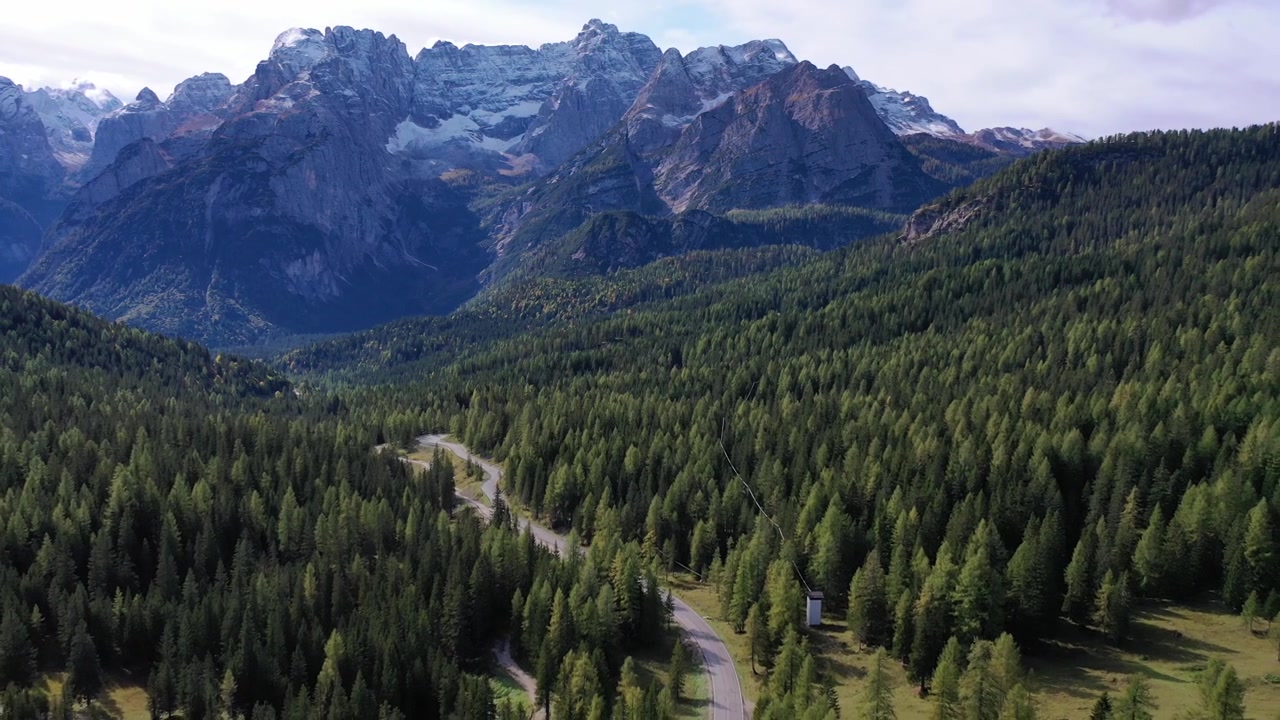 Splendida ripresa aerea con drone dall'alto della scoscesa cima del Monte Pelmo nelle Dolomiti italiane. Caratterizzata da formazioni rocciose spolverate di neve, nuvole basse nella valle e una calda luce del tramonto all'ora d'oro.