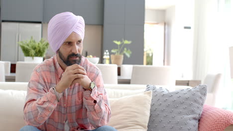 sitting on couch, thoughtful indian man in turban relaxing at home
