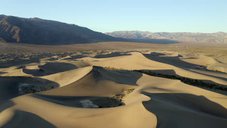 High,-drone-aerial-shot-of-empty-sand-dunes-in-the-desert,-with-mountains-in-background-golden-hour,-sunset