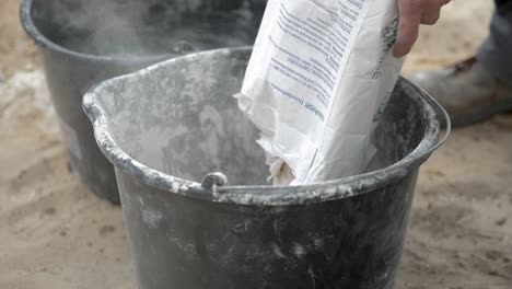 pouring a bag of lime mortar into bucket for mixing