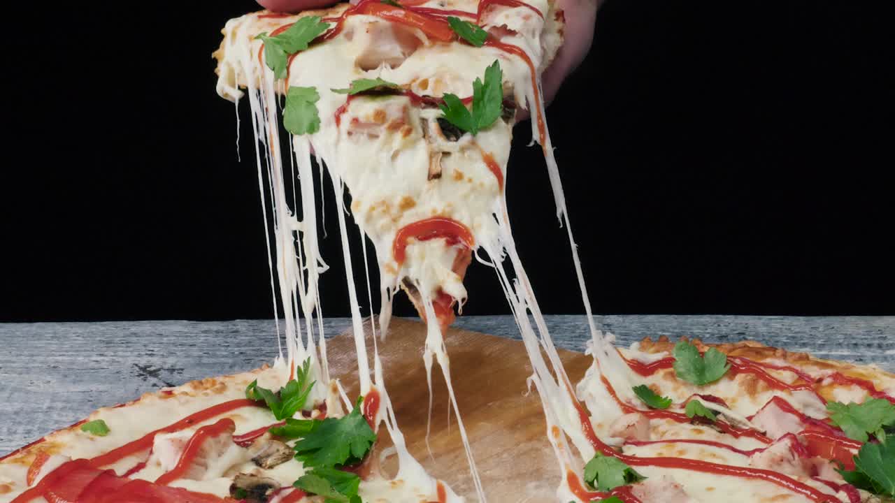 Hand holding a slice of pizza with melted cheese
