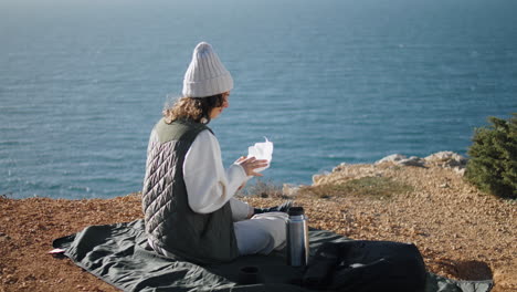 Girl-rest-ocean-cliff-picnic-on-vacation-vertical.-Carefree-tourist-admire-view