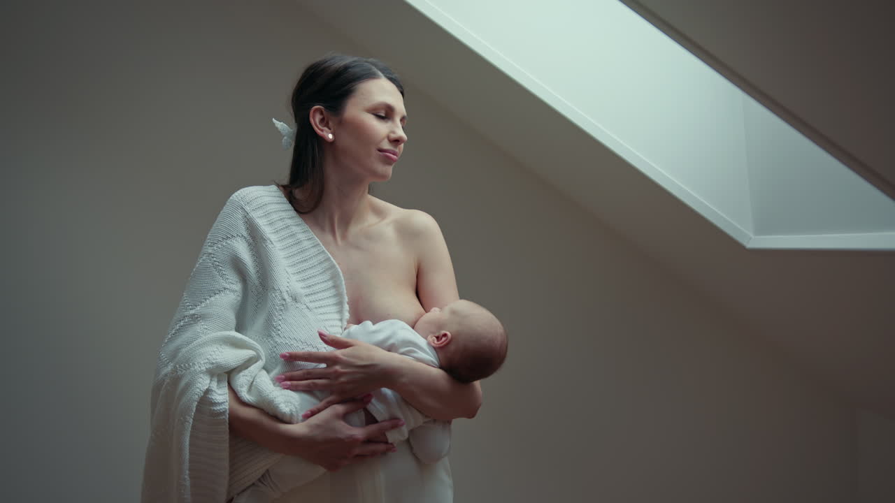 Madre amamantando a bebé recién nacido en interiores con luz suave, vínculo tierno, mujer, padre, hijo, familia, amor