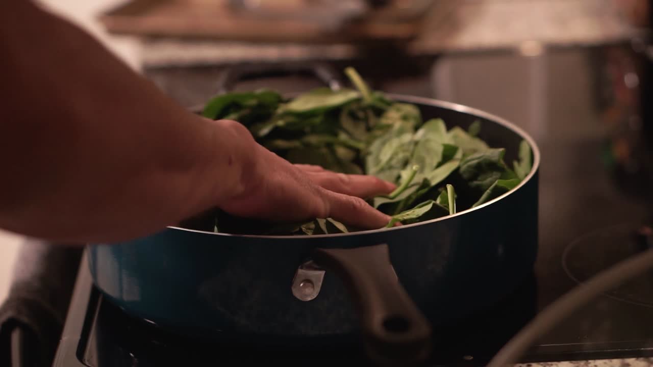 smashing spinach into blue pan on glass stove top and pick up around the pan