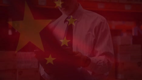 Animation-of-chinese-flag-waving-over-man-using-tablet-in-warahouse
