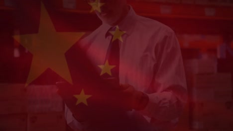 animation of chinese flag waving over man using tablet in warahouse