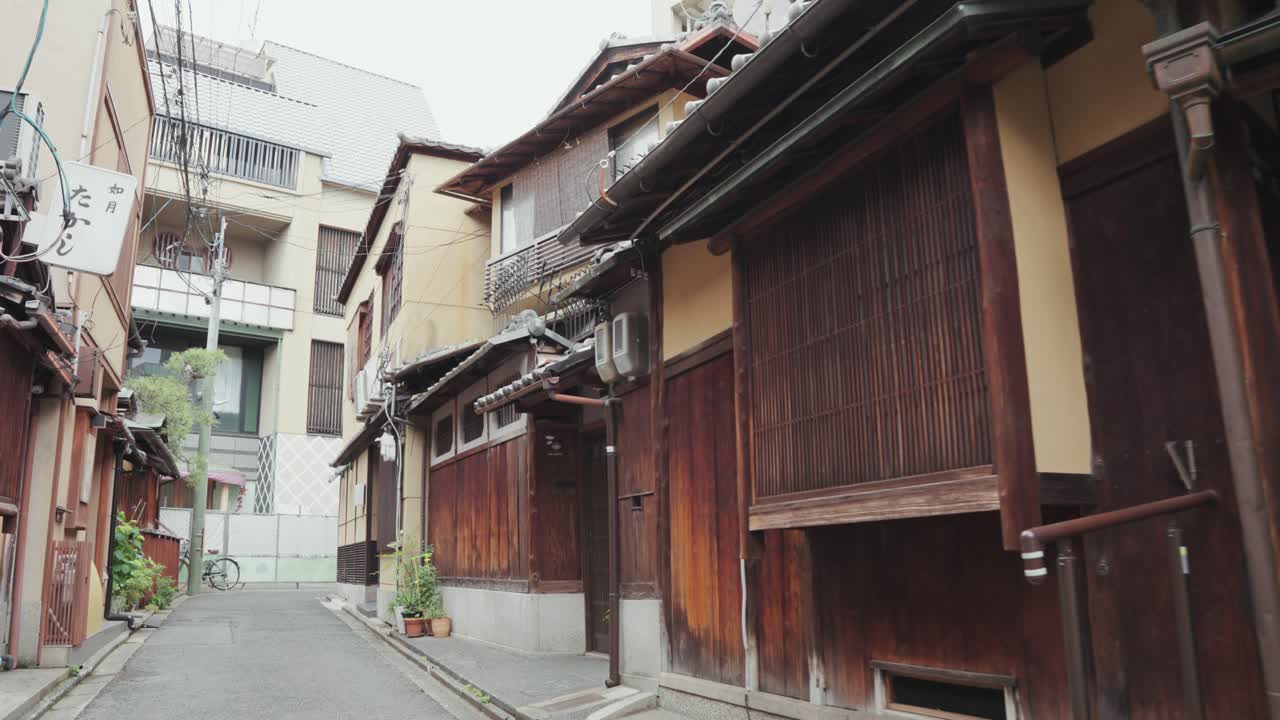 A peaceful daytime walk through a charming Kyoto alleyway, surrounded by traditional wooden buildings, quaint shops, and locals enjoying the serene yet vibrant atmosphere of the historic city.
