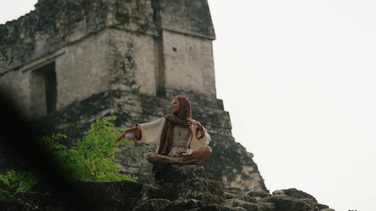 A woman meditates in a spiritual posture in front of a Mayan pyramid at the Tikal ruins in Petén, Guatemala.