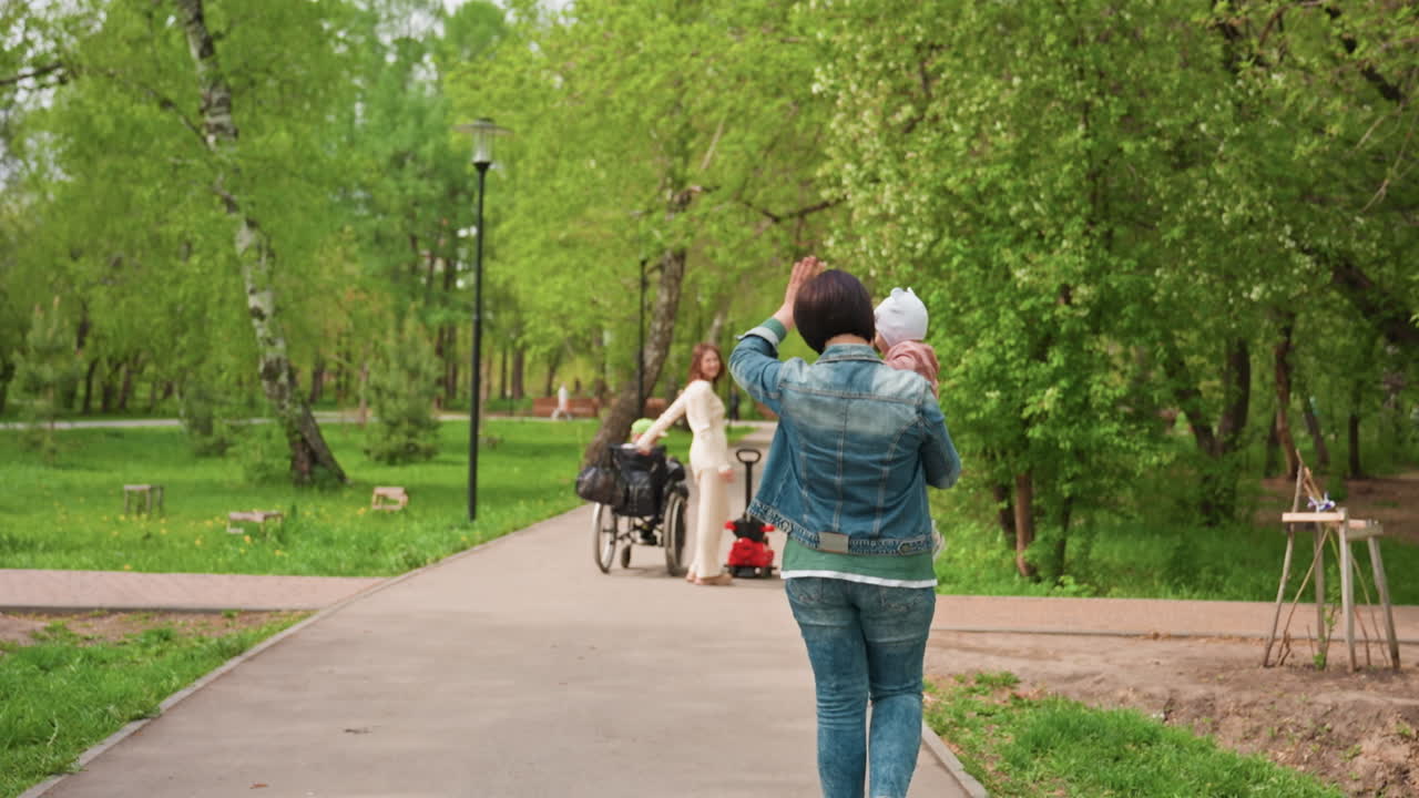 Path Approach Capturing Close Family Moment With Wheelchair And Baby, Adult Walking Forward In Denim, Gentle Conversation Near Bench, Inclusive Scene, Leafy Background, Neighborhood Park Energy