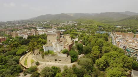 Aerial View of Historic Castle Nestled Among Green Trees with City and Mountains in Background