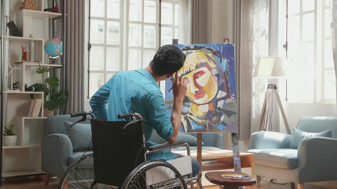 vista posterior de un artista asiático en silla de ruedas sosteniendo un pincel de colores mixtos y pintando la cara de una niña en el lienzo