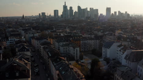 Sich-Vorwärts-Bewegende-Und-Aufsteigende-Drohnenluftaufnahme-Der-Stadtnachbarschaft-Und-Der-Wolkenkratzer-In-Der-Ferne.-Skyline-Der-Innenstadt-Gegen-Sonne.-Frankfurt-Am-Main,-Deutschland